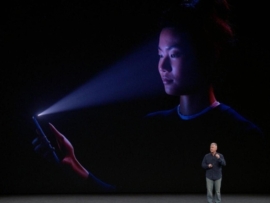 Man standing on stage in front of a giant screen showing a woman using an iPhone to scan her face